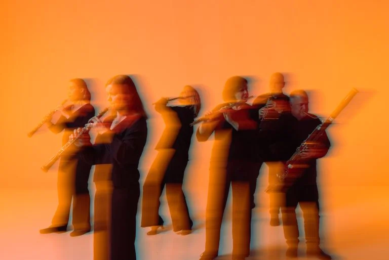 Puupuhallinsoittajat soittavat oranssilla taustalla.