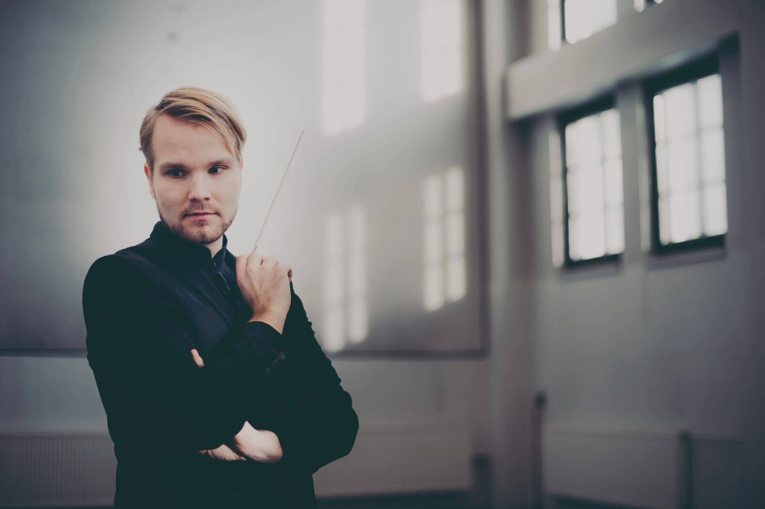 Henkilö seisoo suurten ikkunoiden valossa kapellimestarin puikko kädessään.